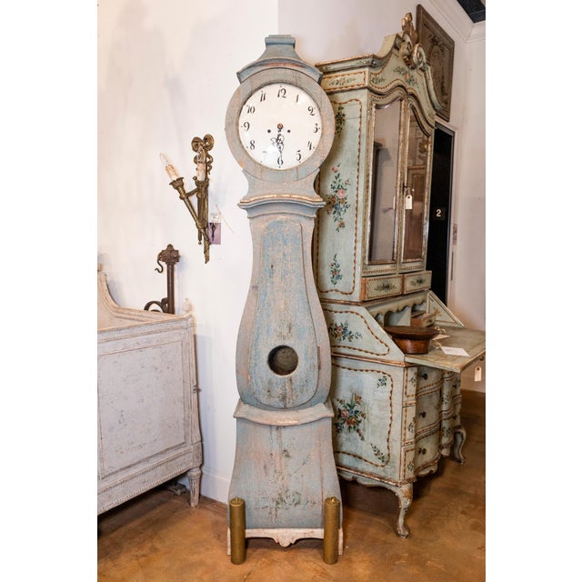 A Swedish painted wood Mora clock from circa 1790s with carved crest, blue gray painted finish and single door. This...