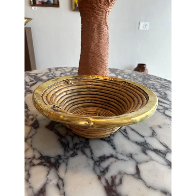 A vintage pencil reed rattan bowl with brass trim, defined by its coiled construction and warm natural tone. The form is...
