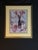 Framed floral still life artwork featuring flowers, fruit, glassware, and a table setting in a classic decorative style....
