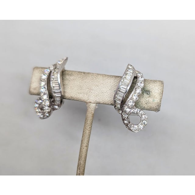 1960s rhodium plated baguette and round clear rhinestone swirl clip earrings. Marked "KRAMER©" on the clips. Measure: 1...
