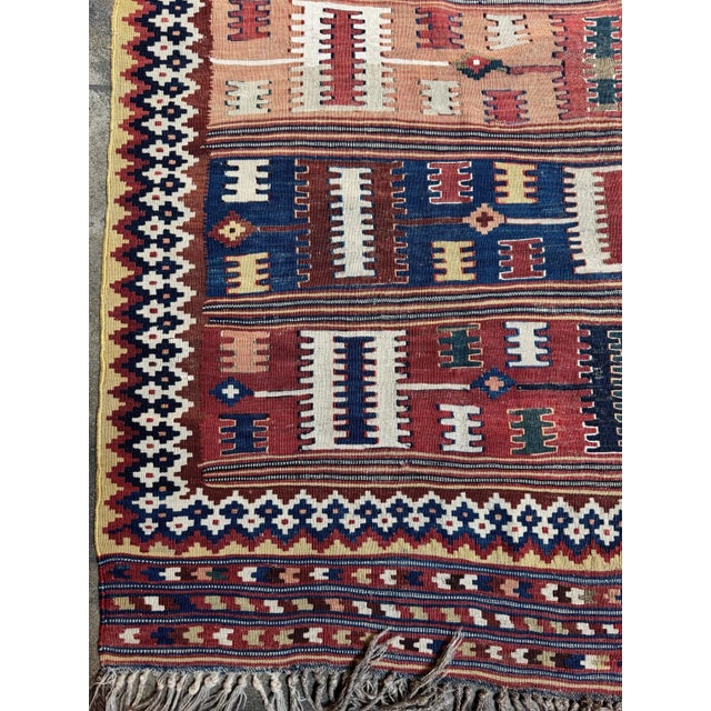 This vibrant vintage Ghashghai Kilim rug features bold horizontal tribal bands in an array of warm earth tones, rich reds,...