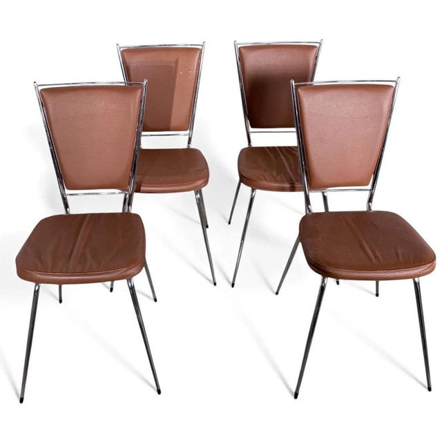 These chrome dining chairs are a set of four vintage 1970s French chairs featuring tan brown leatherette upholstery,...
