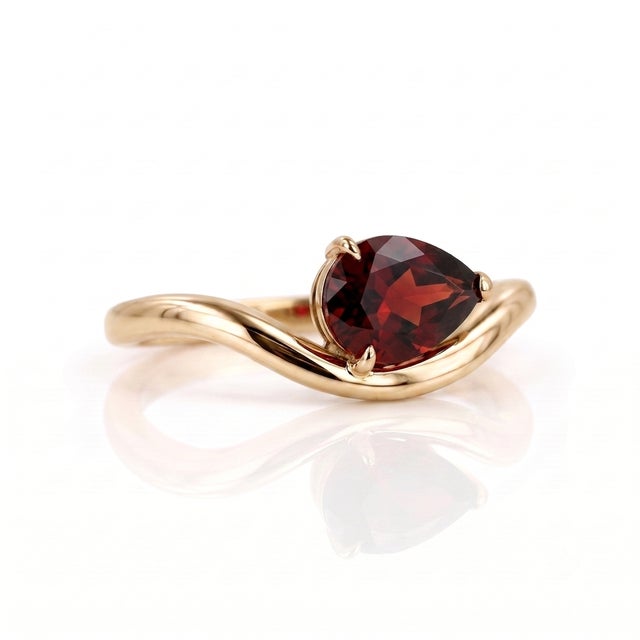 Indulge in the dramatic beauty of this deep red, pear-shaped Garnet ring. The 7x5mm solitaire gemstone is nestled...