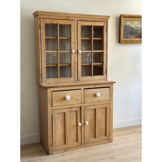 A two-part English pine hutch in warm honey — the upper section enclosed behind a pair of six-pane glazed doors with cup...