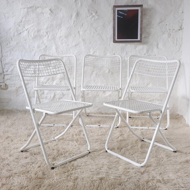 Five tubular steel chairs with mesh seats and backs, all white. They fold using a telescopic system and have non-slip...