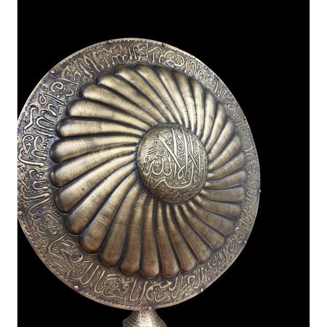 A handmade brass armor display featuring a domed helmet and round shield mounted together on a matching pedestal stand....