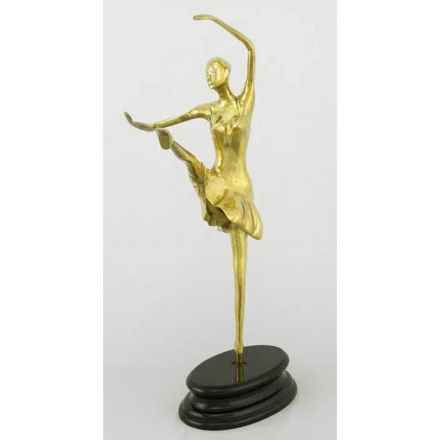 Brass sculpture of a ballerina in motion, on a black lacquered turned wood base.