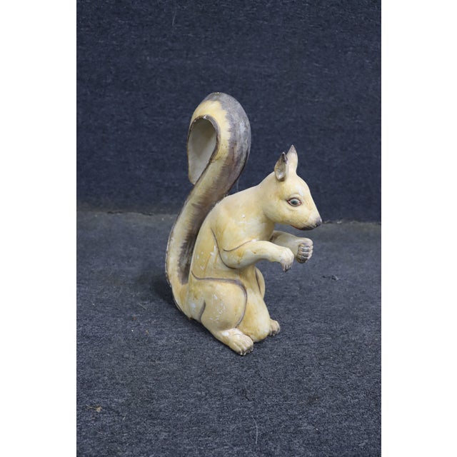 Folk art wooden squirrel figure with a curled tail and hand-painted details in muted yellow, brown, and cream tones....