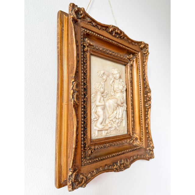 A framed classical figural relief wall plaque in a rococo revival style frame. the composition evokes a quiet, intimate...