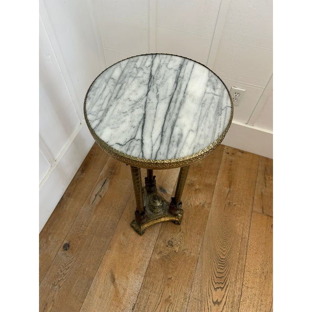 Vintage pedestal with a white and gray marble top and ornate brass base. Features three fluted legs with decorative...