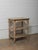 A wooden table with two lower shelves, showing a layered surface built through long use and exposure. The rectangular top...