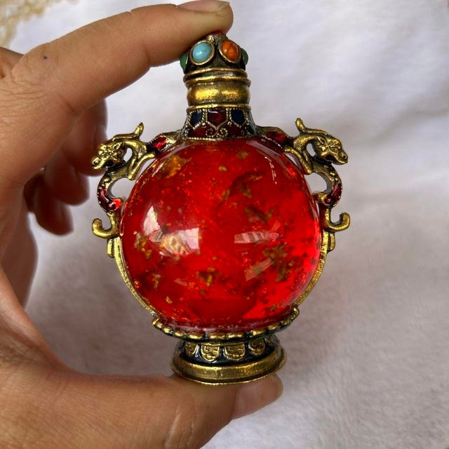 This is a vintage snuff bottle crafted from vibrant red glass with a textured, speckled interior. The bottle is encased in...