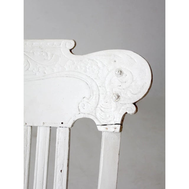 This large antique wooden rocking chair features a timeworn white finish that adds to its character. Designed with a...