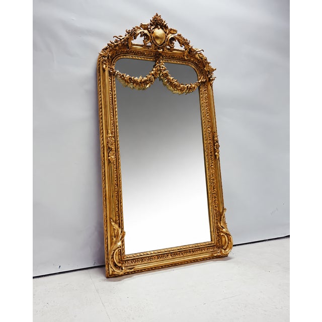 Large gold Baroque mirror with a richly decorated frame, ornate crest, and decorative floral garland. Thanks to its...