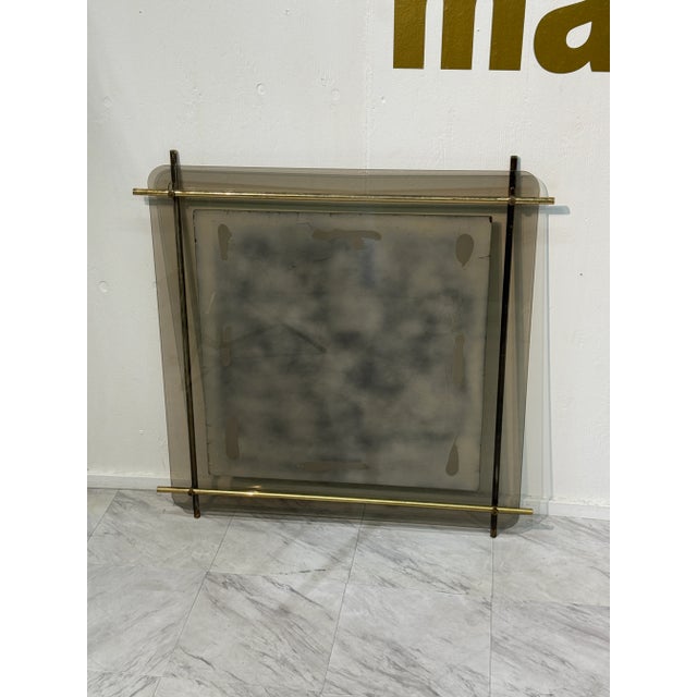 A striking mid-century modern wall mirror featuring a smoked glass border framed with tubular brass rods that extend...