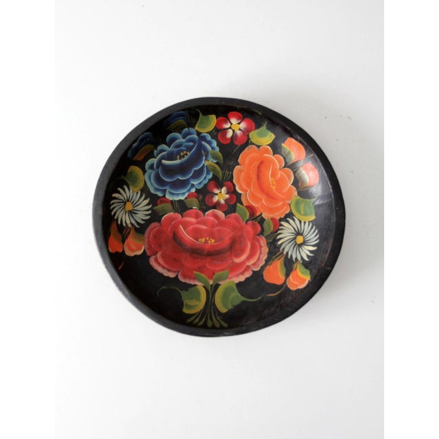 Vintage hand-painted wooden bowl featuring layered folk-art florals in rich shades of red, blue, orange, and cream against...