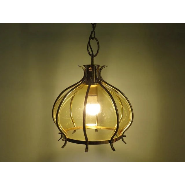 This pendant has an amber-colored chalice set in brass ribs that come together at the top of the fixture. The item is...