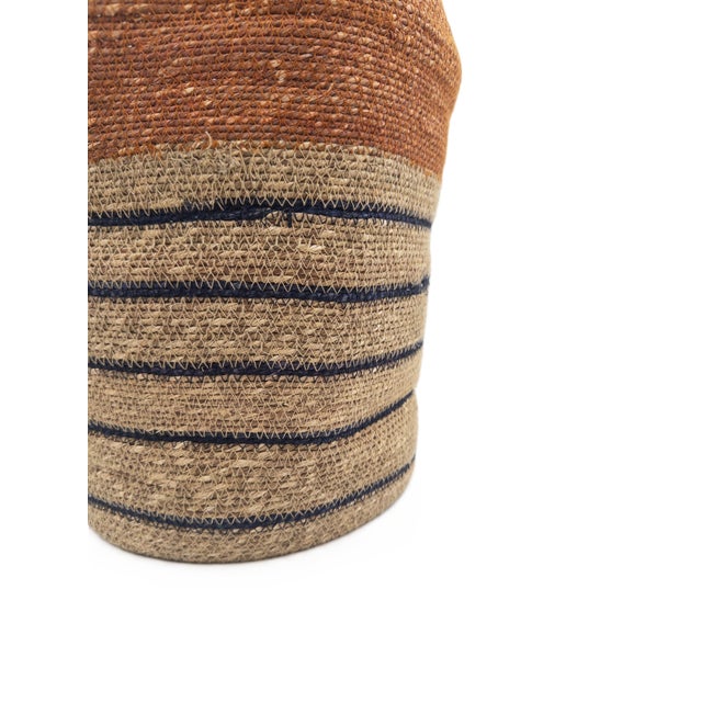 A richly textured handwoven basket crafted in India, featuring a warm terracotta upper band balanced by natural seagrass...