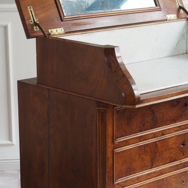 A Louis Philippe washstand, circa 1860, with a hinged top, an integrated mirror, and an inset marble top. The design is...