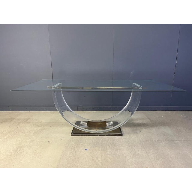 Beautiful hollywood regency dining table. Rectangular glass top mounted on a arched acrylic glass base with a brass foot....