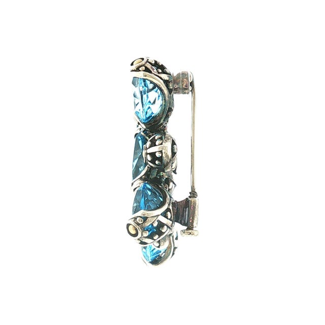 A late 20th-century John Hardy designed brooch featuring 5 round blue topaz stones set in sterling silver and 18k gold....