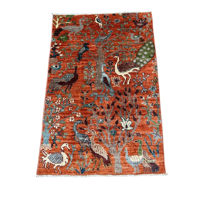 A beautiful pictorial wool rug featuring a peacock and tree of life design in warm orange tones. Its natural dyes and...