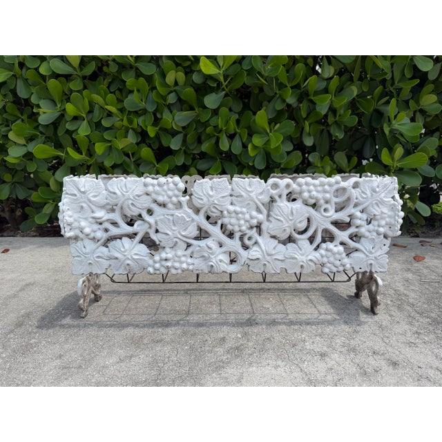 Vintage cast iron jardiniere featuring an ornate grapevine and leaf motif in a white painted finish. The openwork design...