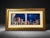 A Mediterranean coastal-style framed wall art piece featuring a dramatic night scene with deep blue tones, moonlight,...