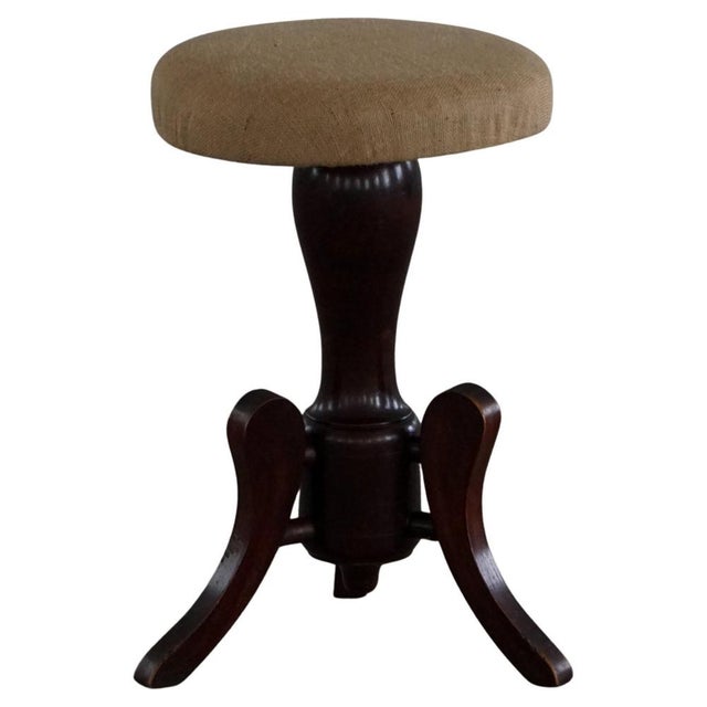 A finely crafted adjustable piano stool, featuring a round, upholstered seat and three elegantly curved cabriole legs...