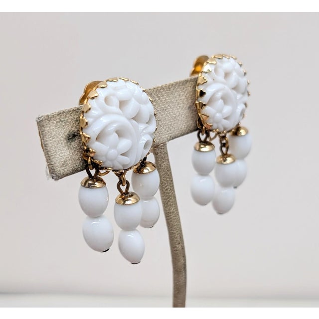 1960s goldtone round carved white faux-jade top with three strands of two white bead drops clip earrings. Marked "NAPIER...
