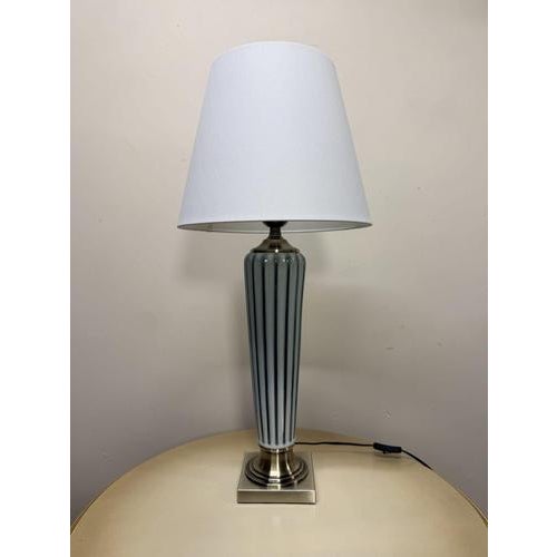 Porcelain and metal contemporary table lamp with a very sophisticated presence. The lamp comes complete with its shade and...