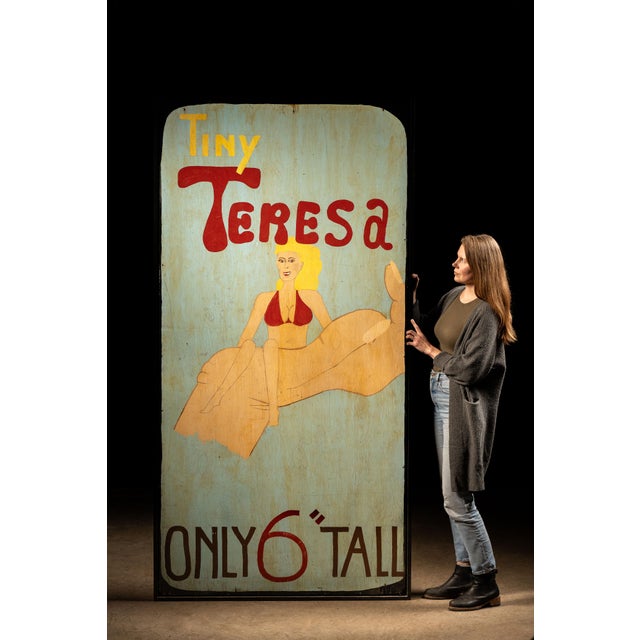 Vintage painted carnival sideshow sign advertising “Tiny Teresa,” a purported six-inch-tall performer shown alongside a...