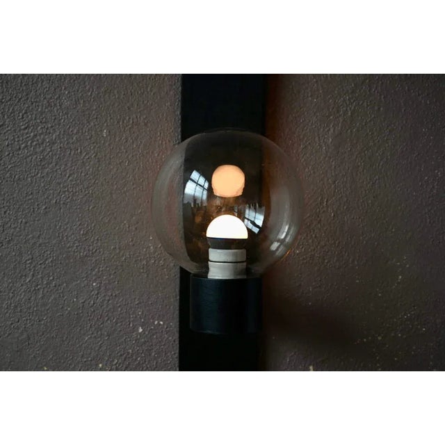 The design of this light wall light is both simple and effective. The black raw metal structure supports a large sphere in...