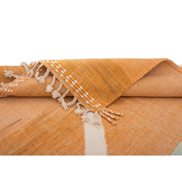 A soft mint house-shaped motif hovers above a graceful cream chevron on a rich burnt orange ground, giving this handwoven...