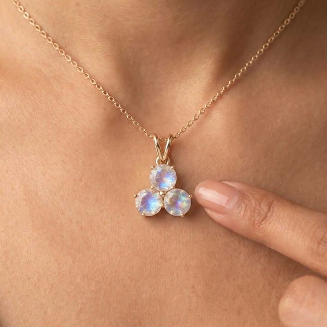 An ethereal three-stone design featuring round-cut natural moonstones arranged in a graceful trefoil formation, secured in...