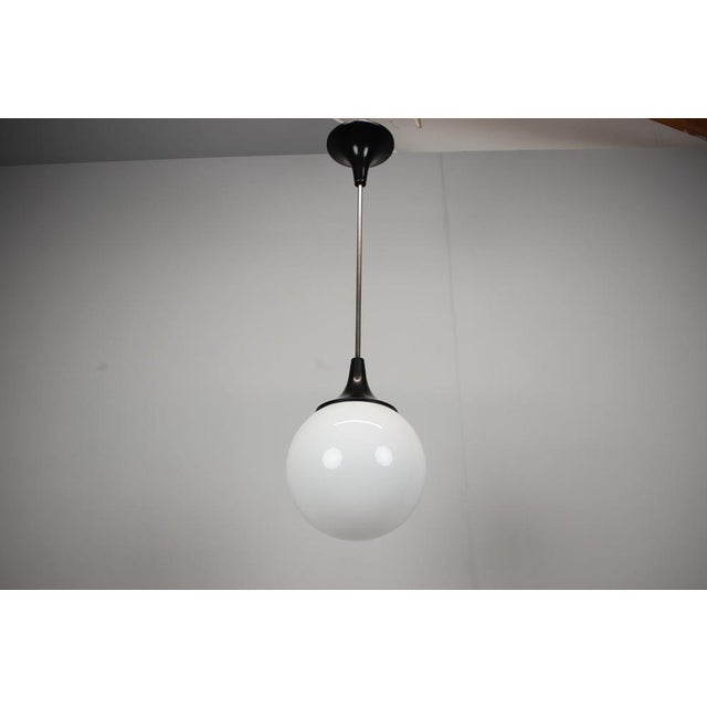 A Czechoslovak pendant lamp from the 1970s featuring an opaline glass globe suspended from a chrome-plated rod with black...
