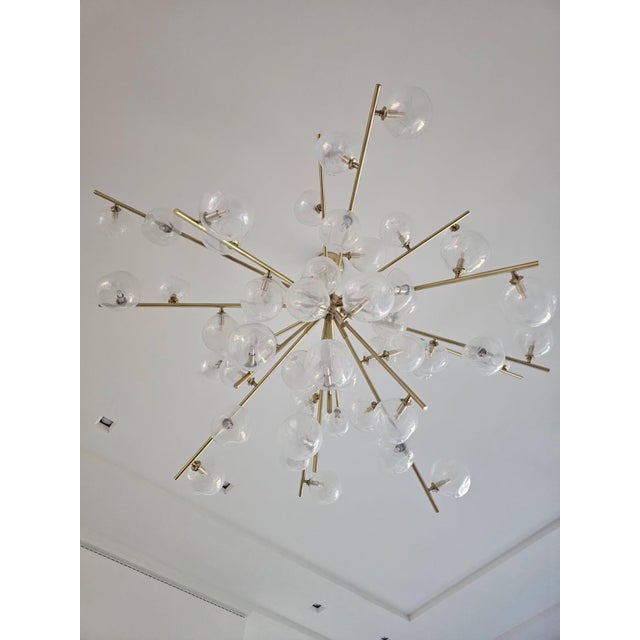 Large custom sculptural chandelier featuring branching brass arms with dozens of floating clear glass globes. Inspired by...