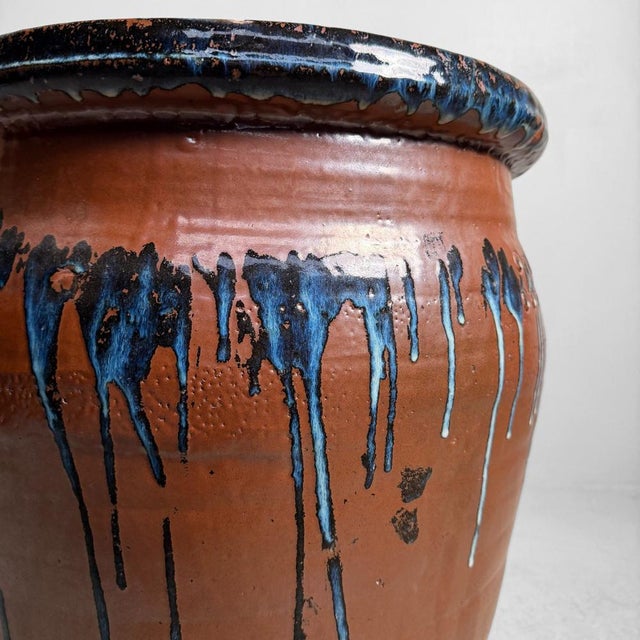 Large Japanese jar made from heavy stoneware, with a warm reddish-brown body and a striking rim and shoulder in dark blue-...