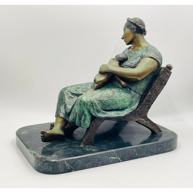 A powerful and intimate bronze sculpture depicting a seated mother cradling her child, created by Martin González Perez, a...