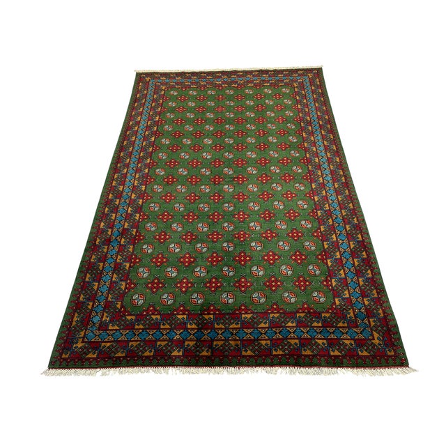 Rows of small octagonal Mori Gul motifs and red geometric flowers repeat across the rich green field of this wool rug....