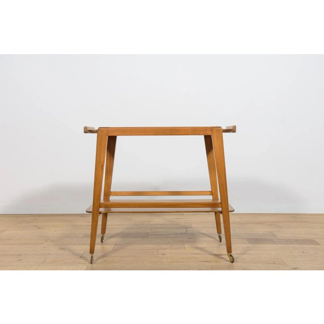 This bar cart was manufactured in the 1960s in Great Britain. The tabletop is made of oak and the frame is made of beech....