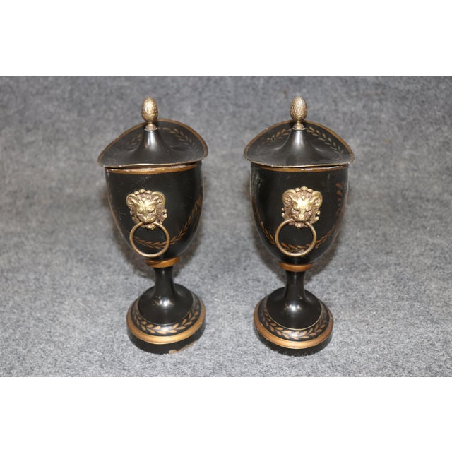 These elegant Neoclassical style metal and brass covered urns are a striking expression of timeless European design,...