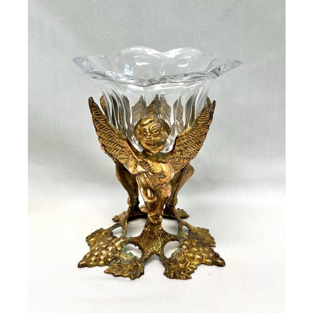 This vintage brass cherub pedestal bowl pairs a detailed gilt-toned figural base with a faceted glass insert for a classic...
