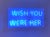 This artwork features a vibrant blue neon sign that boldly states "WISH YOU WERE HERE," creating an inviting yet...
