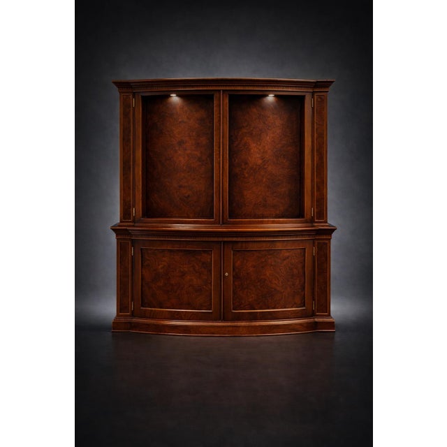 A monumental two-piece Baker Furniture bow front display cabinet featuring a dramatic convex form, dentil crown molding,...