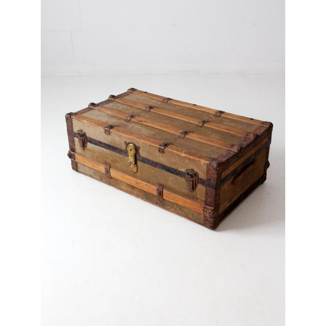 This is an antique steamer trunk. The wooden trunk features a flat top with wood banding, canvas cover, and a metal frame...