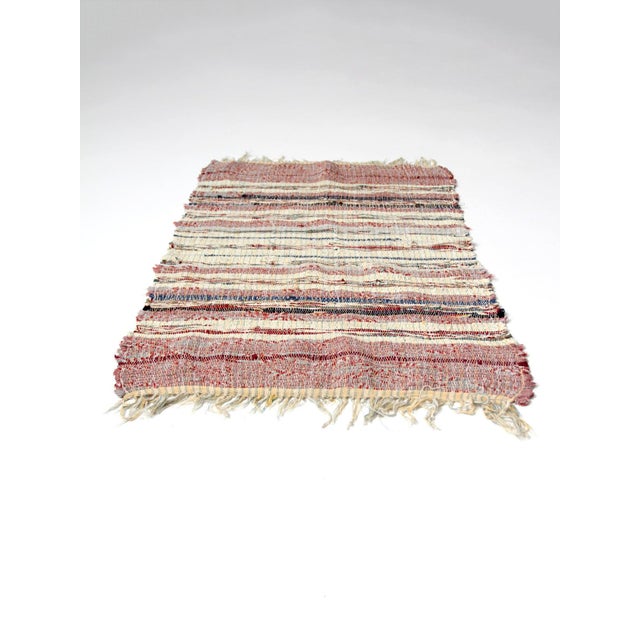 A vintage handmade rag rug in soft tones of red, cream, and blue, circa 1930s–1950s. Woven striping and natural variation...