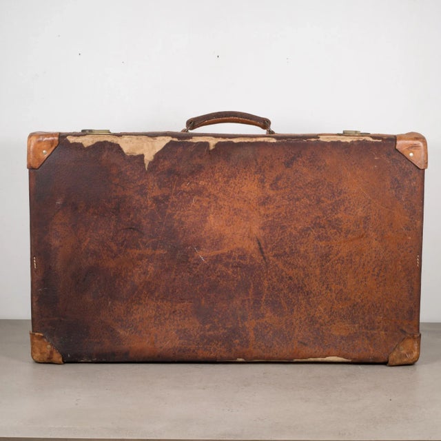 ABOUT A distressed leather suitcase with leather handle, fabric interior and brass locks. Key is missing. CREATOR Unknown....