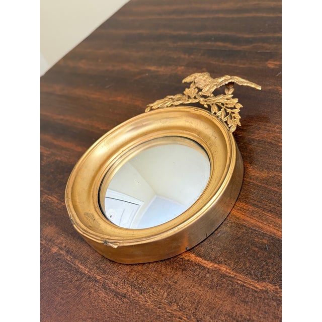 A gorgeous Federal or Regency style small convex bullseye wall mirror featuring an eagle with open wings standing on olive...