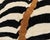 Op art meets gold leaf: hypnotic stripes, split by a single river of ochre. Bold charcoal black and ivory stripes sweep...